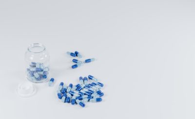A glass jar filled with blue and transparent capsules, with some spilled onto a white surface.