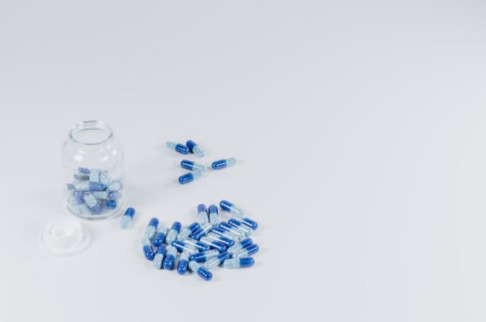 A glass jar filled with blue and transparent capsules, with some spilled onto a white surface.