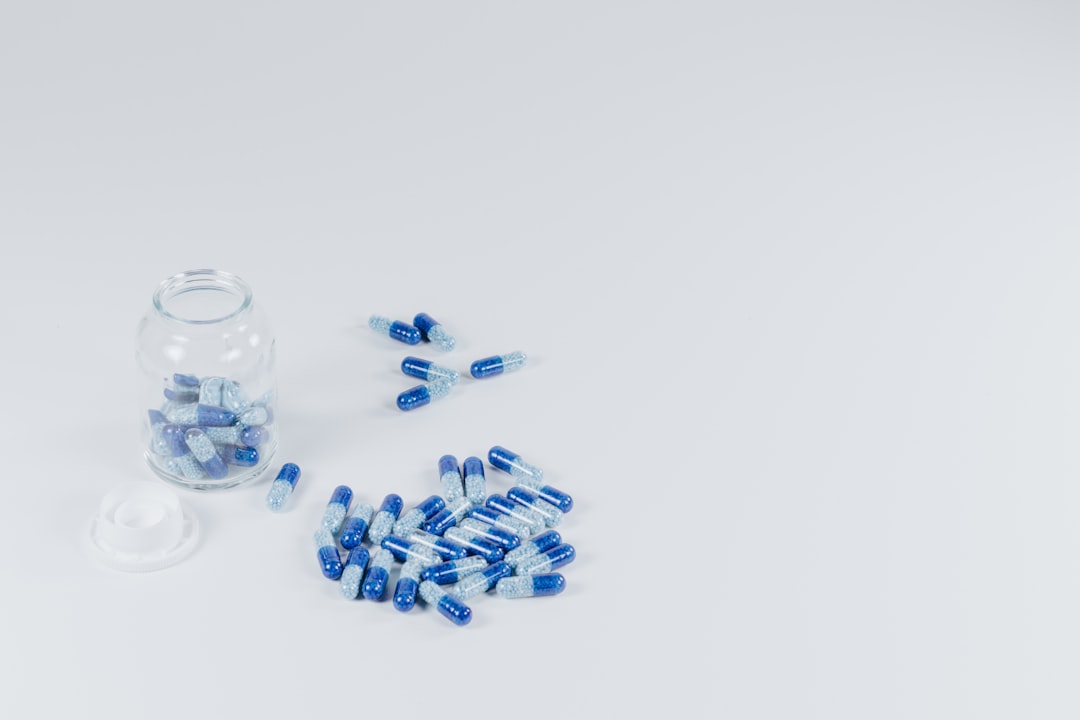 A glass jar filled with blue and transparent capsules, with some spilled onto a white surface.